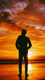 Silhouette man standing on beach against orange sky