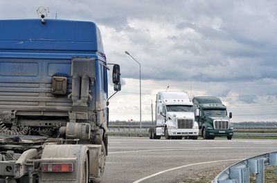 Trucks on road against cloudy sky