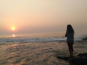 Rear view of woman standing on beach against sky during sunset