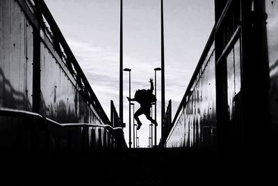 Rear view of silhouette man standing on bridge against sky