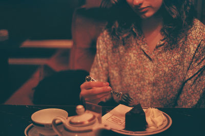 Midsection of woman holding chocolate while sitting on table