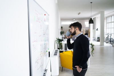 Businessman looking at whiteboard and drinking from mug in office