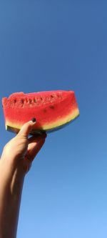 Low angle view of hand holding watermelon against clear blue sky