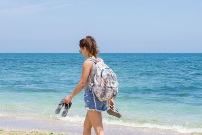 Rear view of woman standing on beach against sky