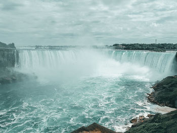 Scenic view of waterfall against cloudy sky