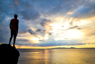 Rear view of silhouette man standing by sea against sky