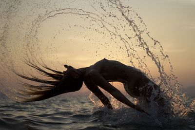 Man splashing water in sea against sky during sunset