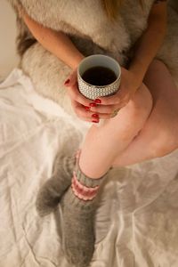 Midsection of woman holding coffee cup on bed