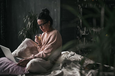 Young woman using mobile phone while sitting on bed