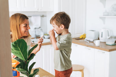 Young woman mother and toddler boy son have fun while cooking with flour at table in bright kitchen 