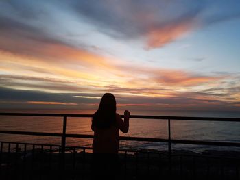 Silhouette woman standing by railing against sea during sunset