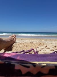 Low section of woman relaxing on beach against clear blue sky