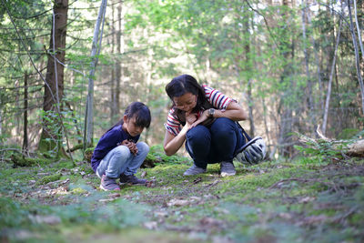 Mother and daughter squatting on a moss covered forest floor looking for insects