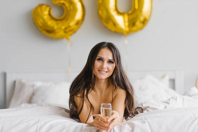 Long haired birthday woman lies on the bed in the morning and holds a glass of champagne 