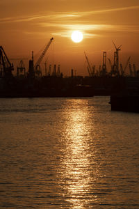 Silhouette cranes at commercial dock against sky during sunset