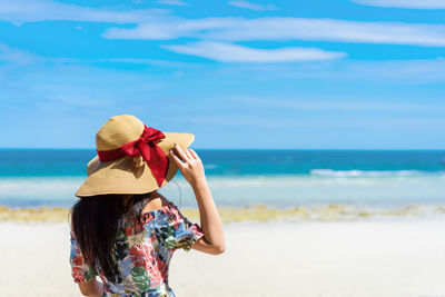 Rear view of woman standing at beach against sky