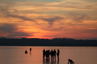 Silhouette people on landscape against sky during sunset