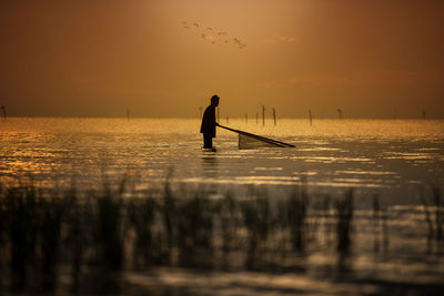 Silhouette man fishing in sea against sky during sunset