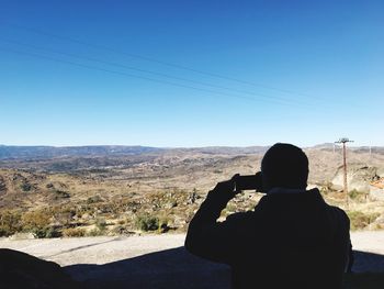 Rear view of woman photographing on landscape against sky