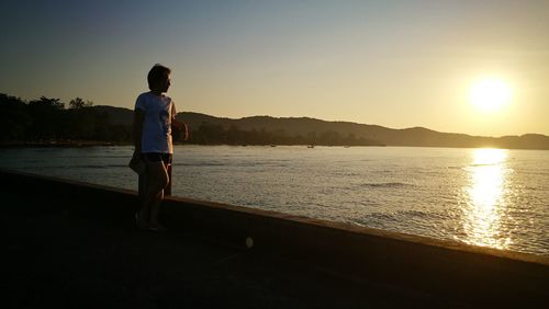 Man standing on sea against sky during sunset