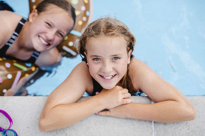 High angle portrait of smiling girl leaning at poolside with sister