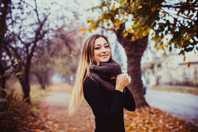 Young woman standing by tree during autumn