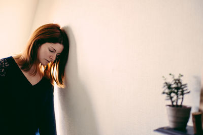 Depressed woman leaning on wall at home