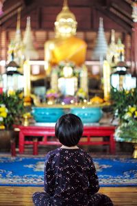 Little girl sits in front of big golden buddha statue at the temple.