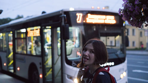 Portrait of young woman sticking out tongue against bus in city