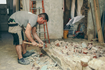 A young man breaks a brick wall with a sledgehammer.