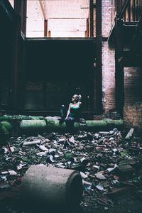 Full length of woman sitting on moss covered pipe in abandoned building