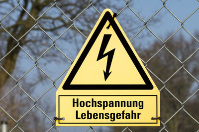 Close-up of high voltage sign on chainlink fence