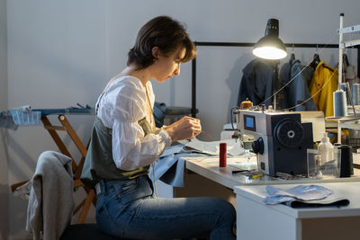 Young female seamstress sew on sewing machine, tailor sit at workplace in fashion workshop atelier