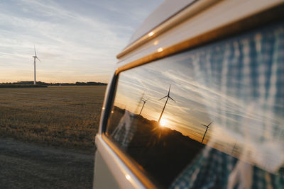 Camper van in rural landscape with wind turbines at sunset