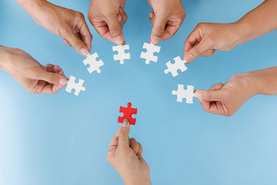 Cropped hand of person holding jigsaw piece against blue background