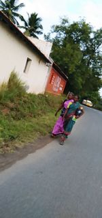 Rear view of woman walking on road by building