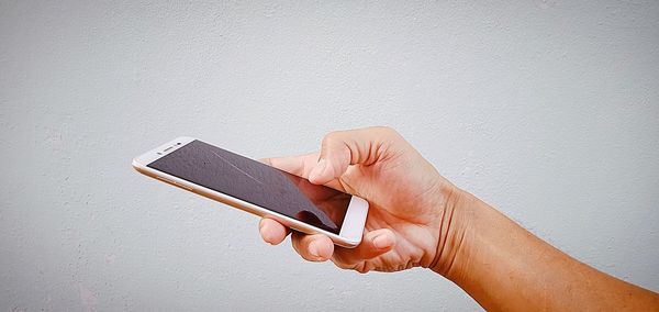 Low section of person holding smart phone against white wall