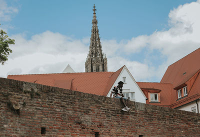 Low angle view of man sitting on retaining wall at church against sky