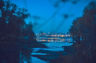 Illuminated buildings by river against sky at night