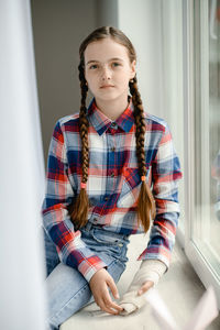 A girl with two pigtails sits on the windowsill by the window. her arm is broken