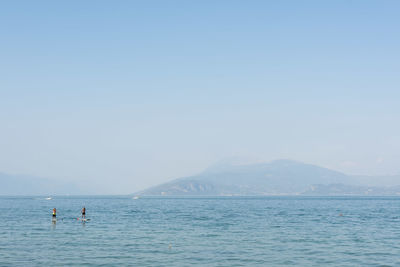 Friends paddleboarding in sea against clear sky