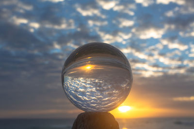 Close-up of crystal ball in sea against sunset sky