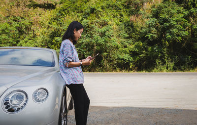 Woman traveler standing next to car trying to get signal on mobile phone.