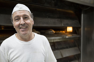 Happy baker with an industrial oven in the background in a bakery