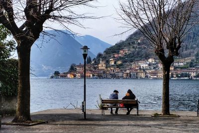 Rear view of people sitting on bench by river