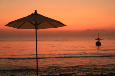 Rear view of woman holding umbrella against sky during sunset