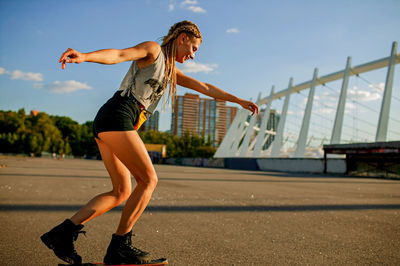 Happy girl with dreadlocks skateboarding in city at sunset.