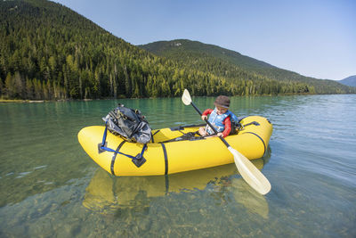 Side vewi of young boy paddling yellow inflatable kayak on calm lake.