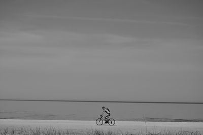 Man riding bicycle on riverbank against sky