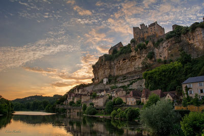 Panoramic view of buildings by lake against sky during sunset